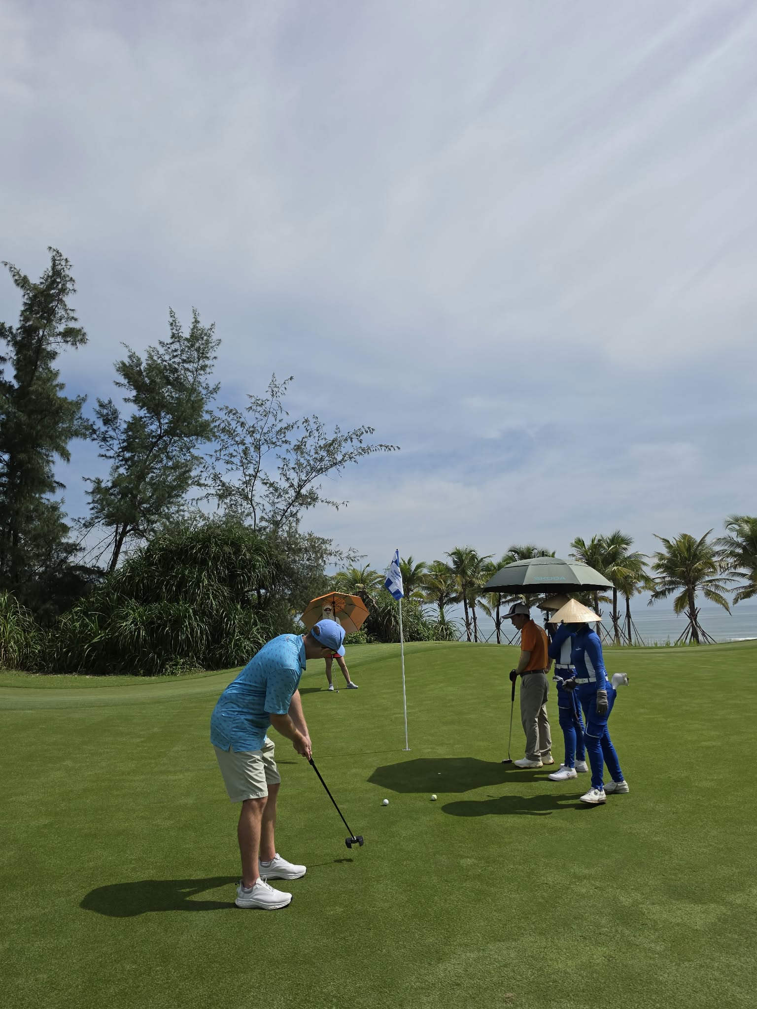 Golfer putting with caddies beside a coastal Vietnam green