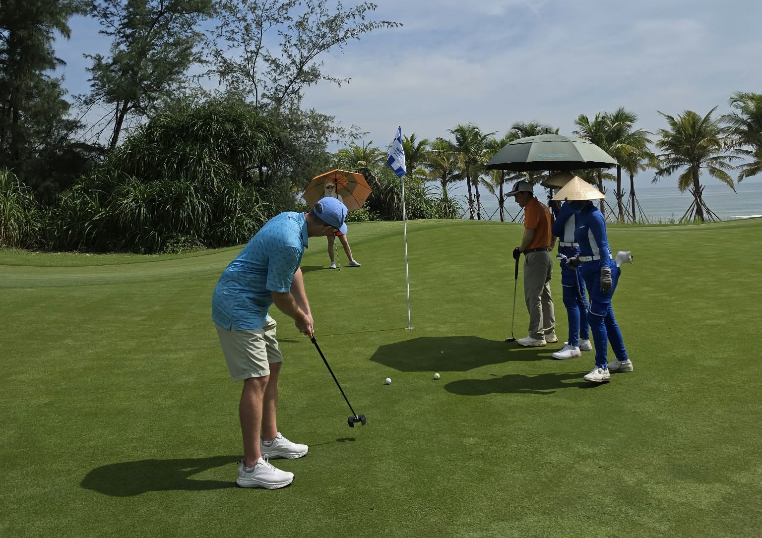 Golfer putting with caddies beside a coastal Vietnam green